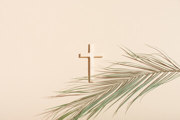 Palm Sunday and Easter concept. Cross or crucifix and palm leaf on light beige background.