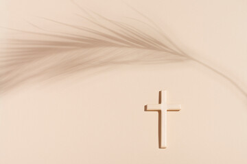 Cross or crucifix and shadow of palm leaf on light beige background. Palm Sunday and Easter concept.
