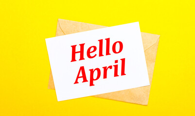 On a yellow background, an envelope and a card with the text HELLO APRIL. View from above