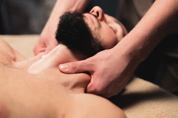 Fototapeta na wymiar Close-up Professional neck massage to a bearded male athlete in a dark room of a spa massage room