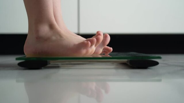 A little girl gets bare feet on the scales. White living room. The concept of weight loss and excess weight in children. Good and correct weight for the child. The legs of the child on the scales