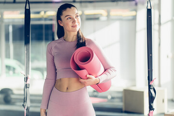 Young woman with slim healthy body standing with pink yoga mat in studio. Fitness female model in sportswear after yoga workout on fitness studio background.