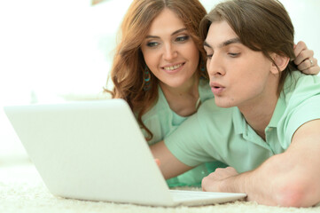 Fototapeta premium Portrait of happy young couple looking at laptop while lying on floor