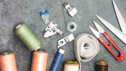 sewing tools : scissors, colorful bobbins with thread and presser foot on gray wooden table