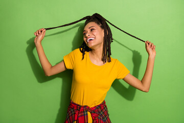 Naklejka premium Portrait of attractive cheerful carefree girl having fun pulling braids isolated over bright green color background