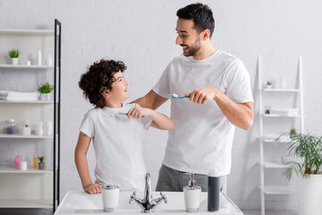 Fototapeta premium Young arabian man looking at son with toothbrush in bathroom