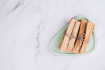 Palo Santo tree sticks on green concrete tray on light marble background - holy incense tree from Latin America. Meditation, mental health and personal fulfilment concept. Selective focus