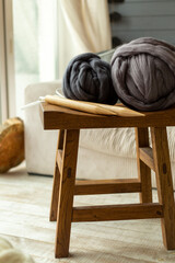 Fototapeta na wymiar Two large balls of merino wool lying on a wooden stool with wooden knitting needles against the background of a window and a white sofa