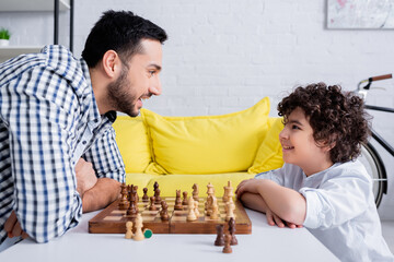 Side view of muslim man smiling at son near chess on board