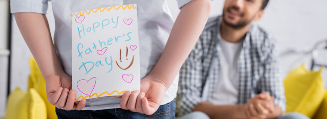 cropped view of kid holding happy fathers day card near muslim dad on blurred background, banner