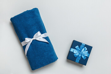 Top view of rolled terry blue towel and gift box on light gray background with copy space.