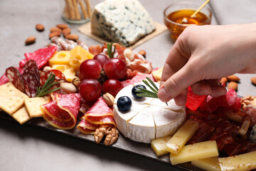Woman putting rosemary on board with different appetizers, closeup