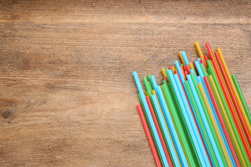 Obraz premium Colorful plastic drinking straws on wooden table, flat lay. Space for text