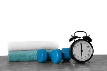 Alarm clock, towels and dumbbells on marble table against grey background. Morning exercise