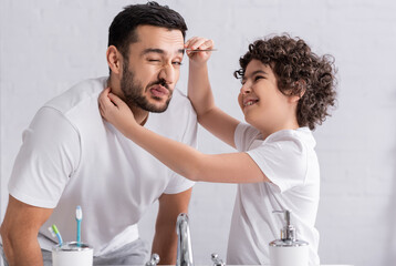Fototapeta premium Smiling muslim boy pulling out eyebrow of father in bathroom