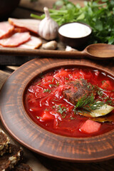 Stylish brown clay plate with Ukrainian borsch served on wooden table, closeup