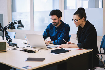 Friendly colleagues working on laptop  and writing comments in notebook in office