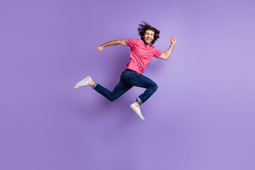 Fototapeta na wymiar Full size profile photo of optimistic nice brunet guy jump wear pink t-shirt jeans isolated on violet background