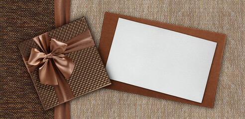 Gift card with gift box with ribbon and bow, isolated on elegant brown fabrics background, top view...