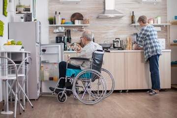 Disabled senior man in wheelchair taking eggs carton from refrigerator for wife in kitchen. Senior...