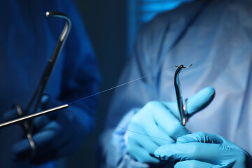 Professional surgeons with forceps and suture thread on blurred background, closeup. Medical...