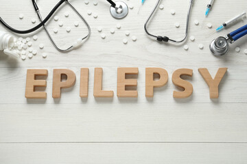 Word Epilepsy made of wooden letters, stethoscopes, pills and syringes on white table, flat lay