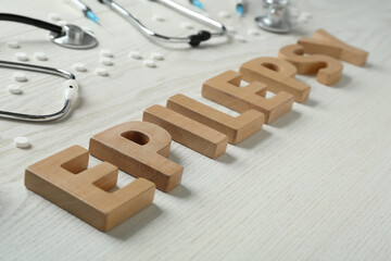 Word Epilepsy made of wooden letters, stethoscopes, pills and syringes on white table, closeup