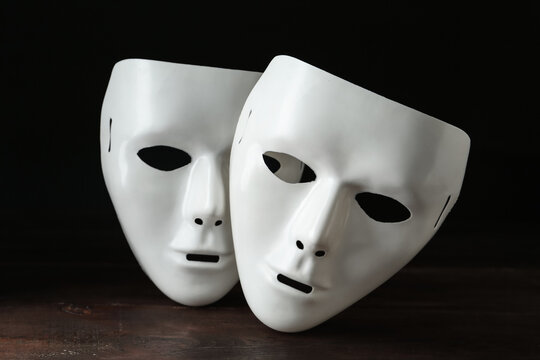 White theatre masks on wooden table against black background