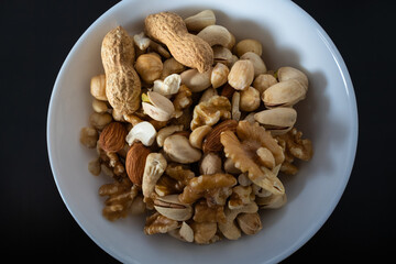mixture of nuts (peanuts, pistachios, almonds, walnuts, hazelnut, cashew) in a bowl from top view with black background