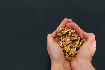 person holding walnuts on his hands with black background and copy space