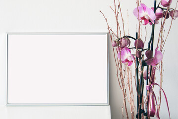silver horizontal empty frame on white table with pink orchid flowers, mockup for arts, photos illustrations