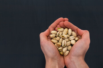 person holding pistachios on his hands with black background and copy space