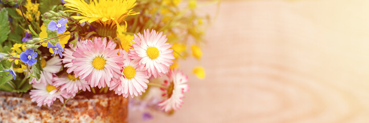 a bouquet of wildflowers of forget-me-nots, daisies and yellow dandelions in full bloom in a rusty rustic jar against a background of wooden planks. cottagecore scene. space for text. banner. flare © Ksenia