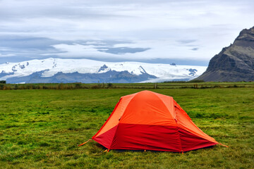 An orange tent in a clearing overlooking the snow-capped mountains. Iceland.