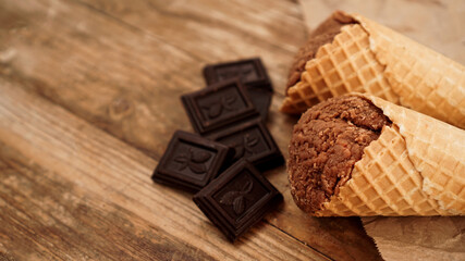 Chocolate ice cream in a waffle cone on craft paper on a wooden background