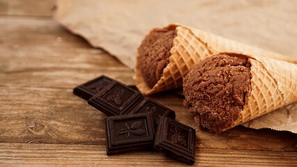 Chocolate ice cream in a waffle cone on craft paper on a wooden background