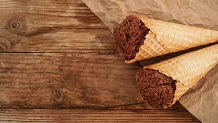 Chocolate ice cream in a waffle cone on craft paper on a wooden background