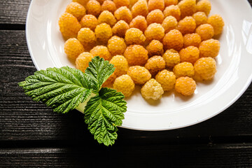 Ripe yellow raspberry lies on a white plate on a black background.