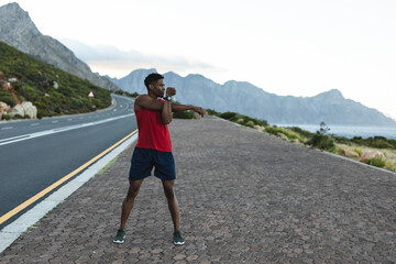African american man exercising outdoors stretching on a coastal road