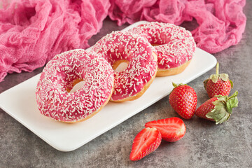 Three appetizing donuts in pink glaze lie on a white plate on a gray background. Junk food.