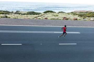 African american man exercising outdoors running on a coastal road