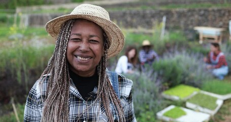 Senior african farmer woman smiling in camera - Gardening people working in background - Farm lifestyle concept - Powered by Adobe