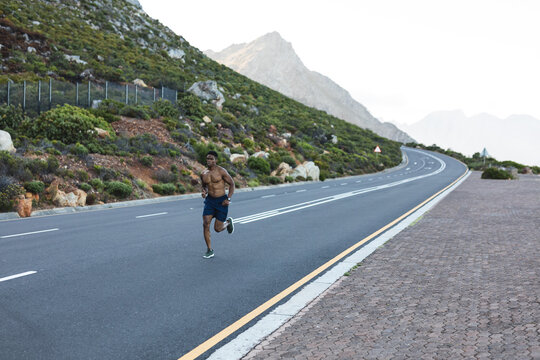 African american man exercising outdoors running on a coastal road - Powered by Adobe