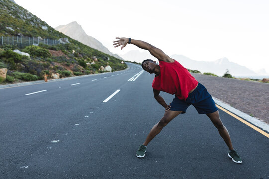 African american man exercising outdoors stretching on a coastal road - Powered by Adobe