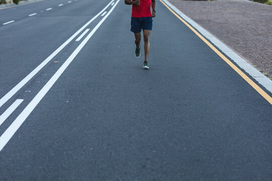 African american man exercising outdoors running on a coastal road - Powered by Adobe