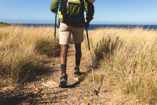 African american man exercising outdoors hiking using walking poles in countryside on a mountain