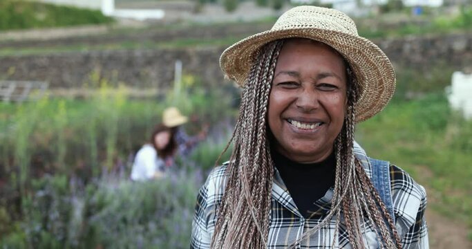 Close up of senior african farmer woman smiling in camera - Gardening people working in background