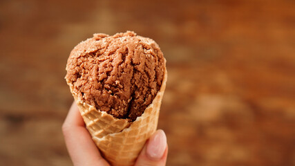 Chocolate ice cream on waffle cone. Wood background. Selective focus.