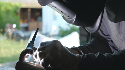 Male mechanic in protective mask doing welds work using professional equipment. Repairman in gloves...