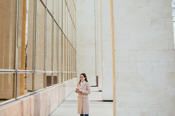 Young pretty woman with eyeglasses near office with panoramic windows drink the coffee at break.